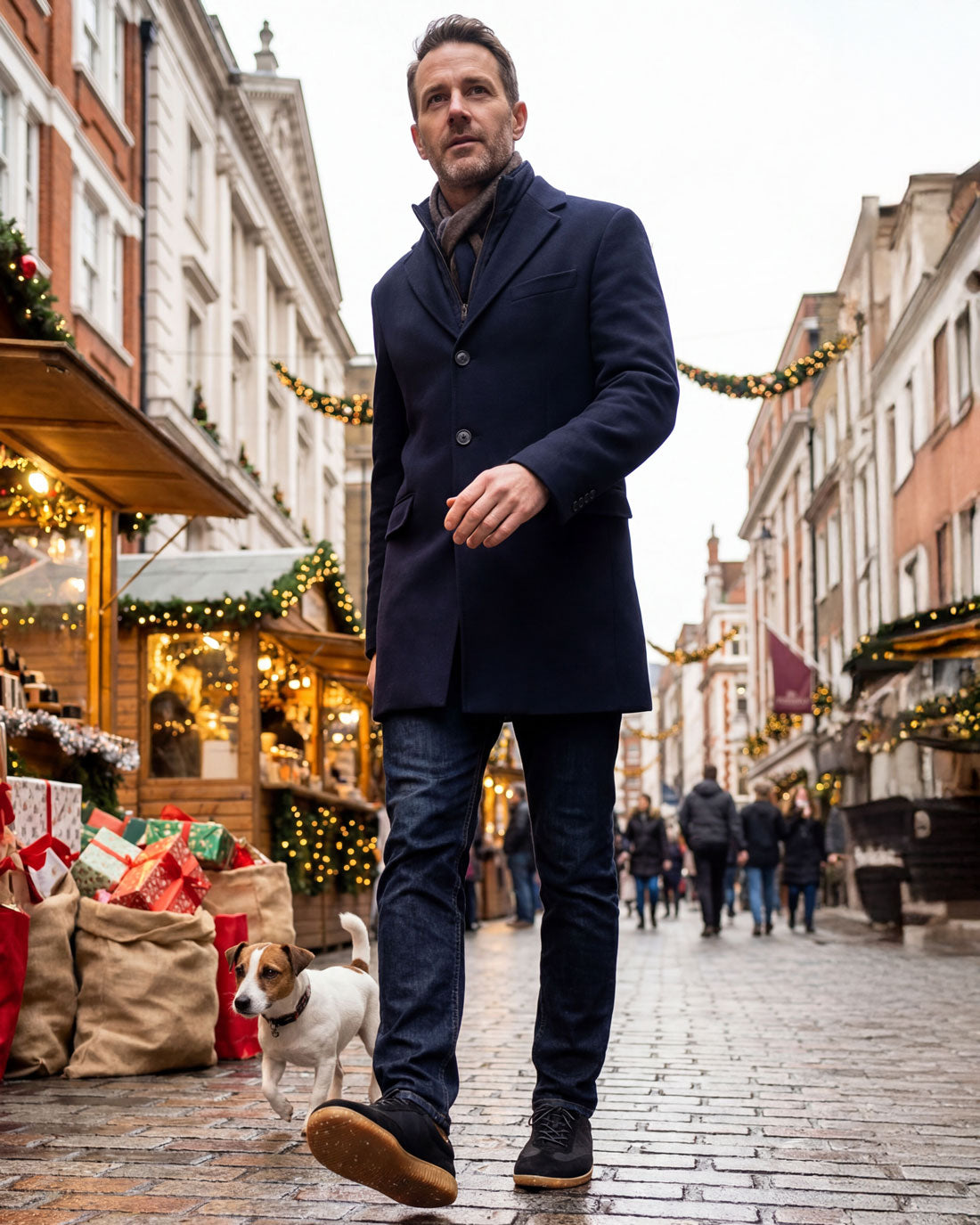 Man wearing Gaucho Ninjas barefoot shoes in a dark coat walking a dog on a festive street with Christmas decorations.