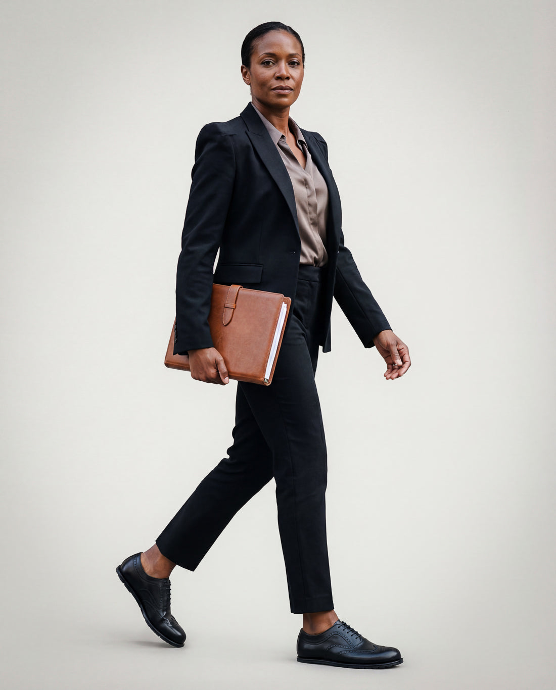 Woman in a professional outfit holding a folder wearing Goodyear welted barefoot brogue shoes in black leather