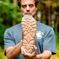 Man holding up a barefoot shoe with a grip sole with a forest background